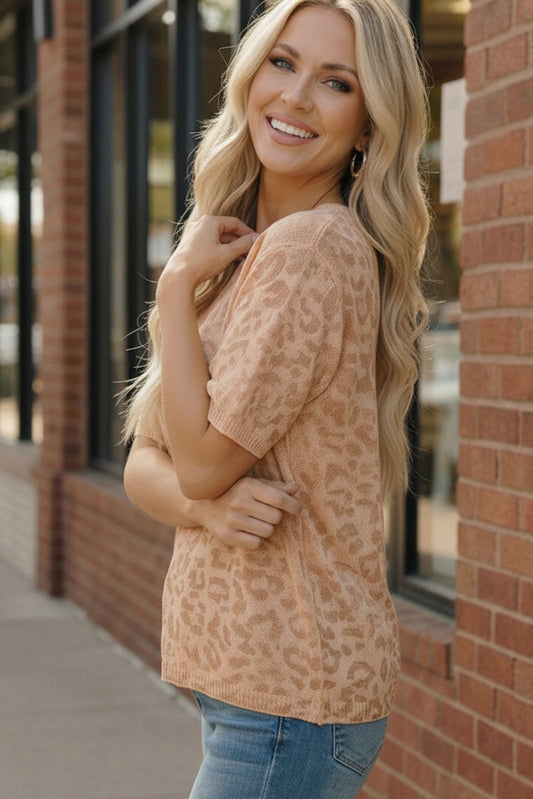 Woman wearing a leopard print top and jeans standing against a brick wall.