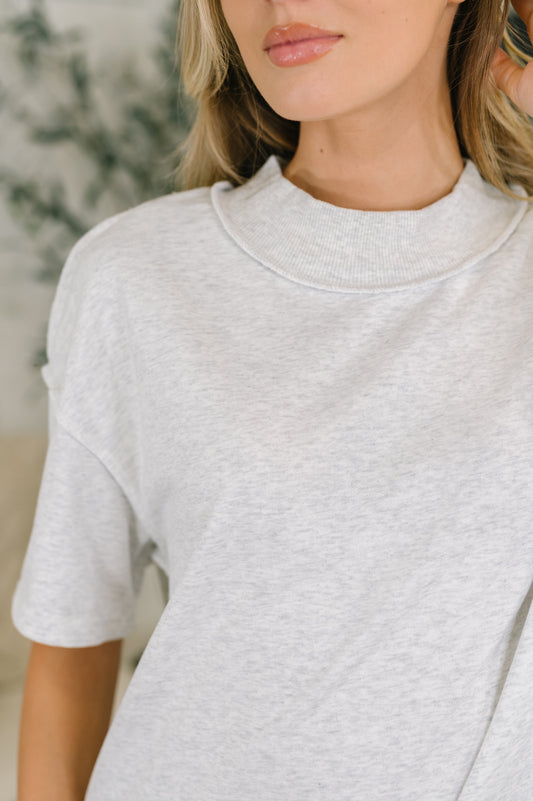 A close-up of a woman wearing a light heather gray short-sleeve mock neck t-shirt.