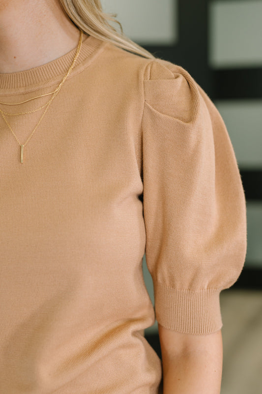 Person wearing a beige sweater with puffed sleeves and a gold necklace.