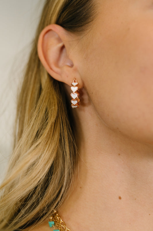 Close-up of a person wearing a rose gold earring with colorful stones.
