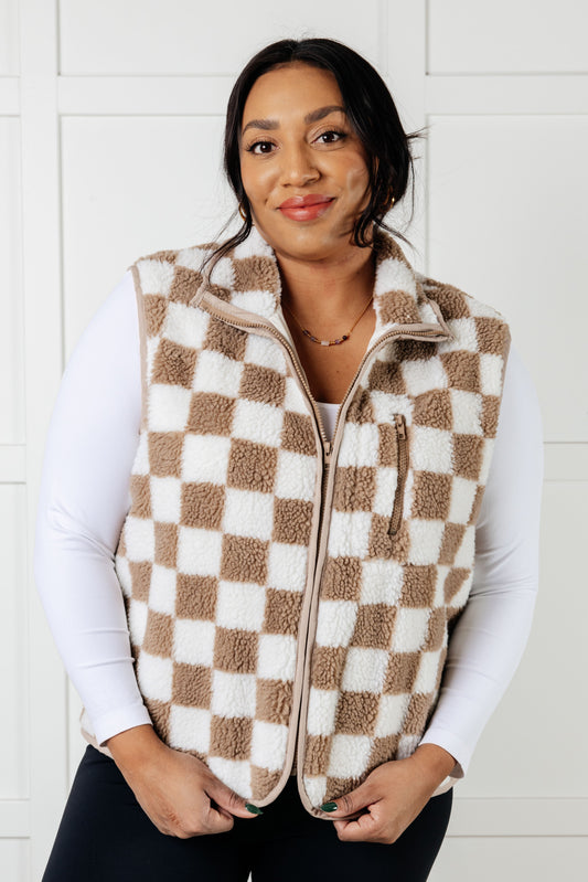 A woman wearing a beige and black checkered fleece vest with a high collar and full front zipper closure, paired with a white long-sleeve top.