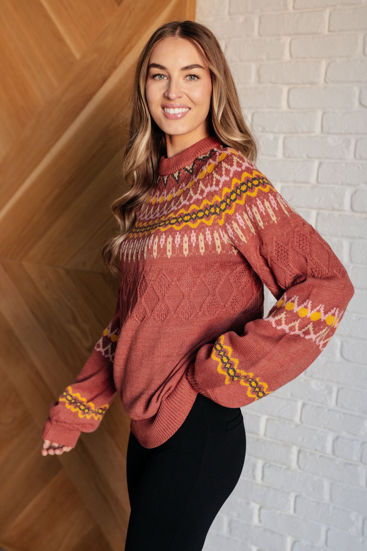 Woman wearing a patterned sweater standing against a brick wall.