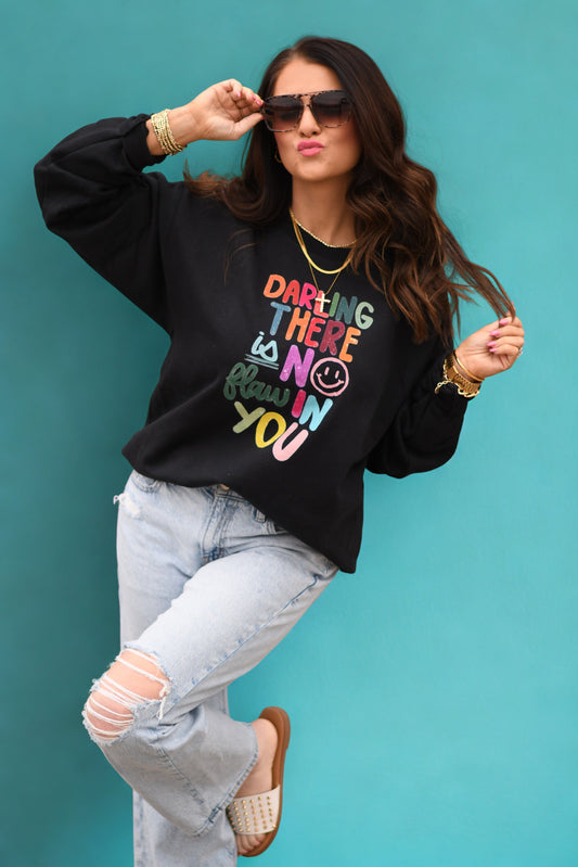 Woman wearing a black sweatshirt with colorful text design against a teal background