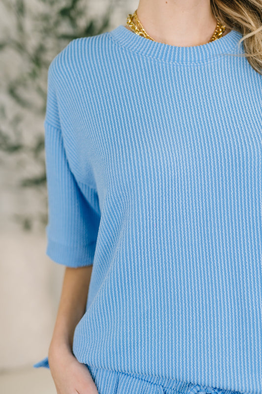 Person wearing a blue ribbed sweater with a blurred background