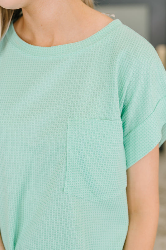 Person wearing a light green textured dress with a blurred background
