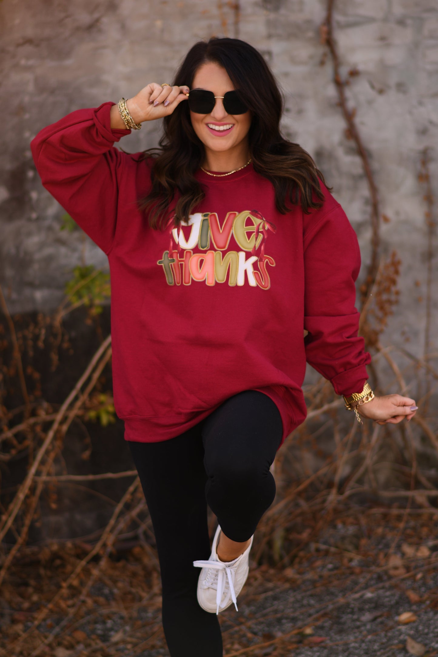 Person wearing a red sweatshirt with colorful text, standing outdoors against a stone wall.