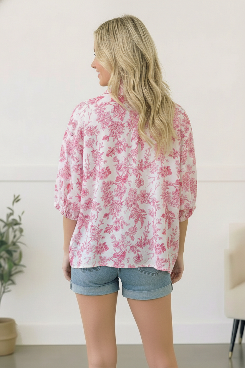 Woman wearing a pink floral blouse and denim shorts in a minimal indoor setting.