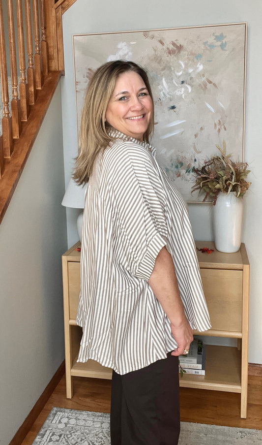 Woman in a striped shirt standing in a room with a wooden cabinet and decorative items.