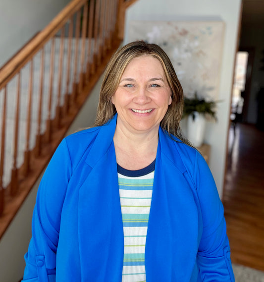 Woman wearing a blue jacket over a striped shirt in a home setting with a staircase.