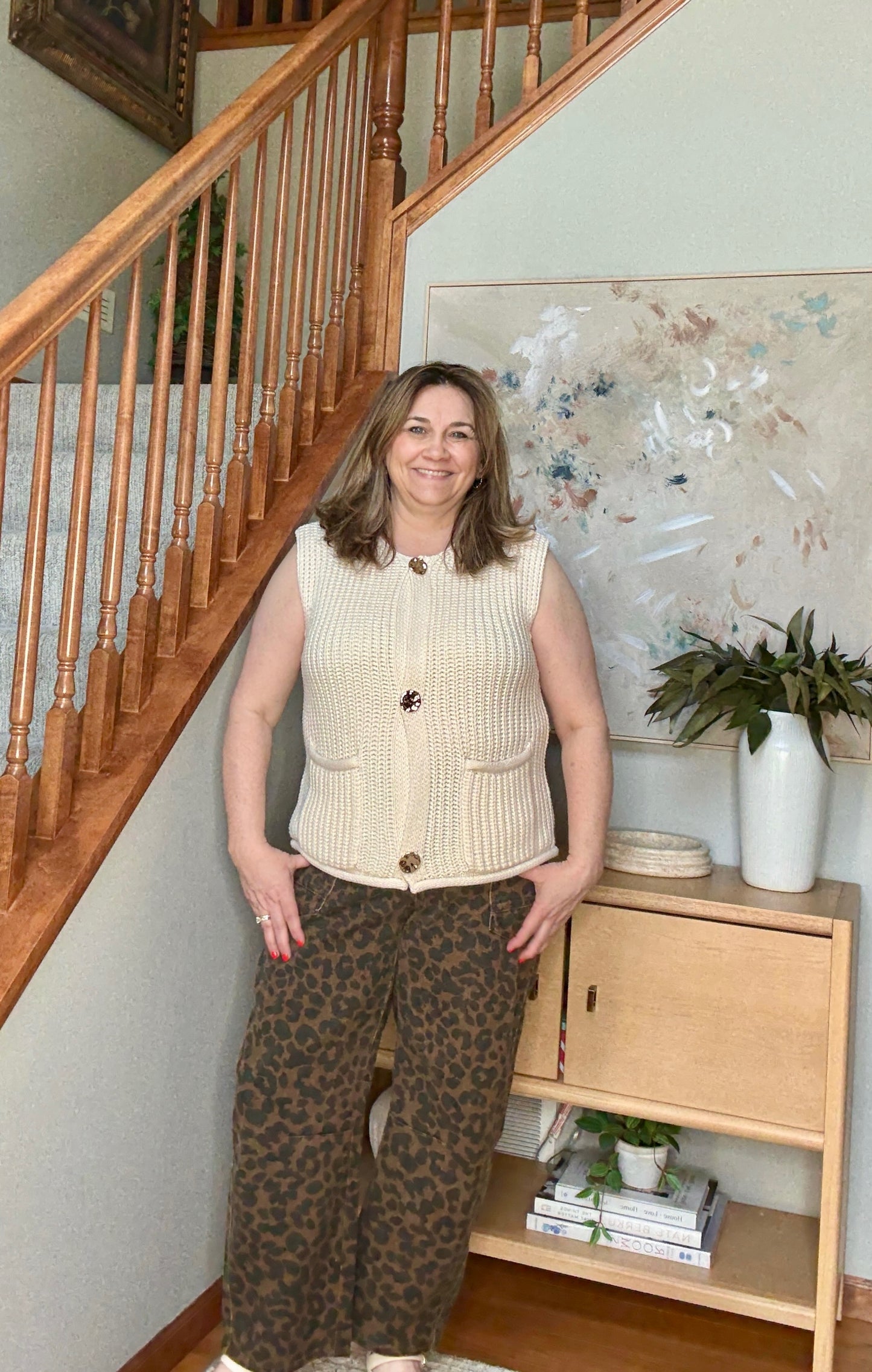 Woman standing in a home setting with a staircase and wooden shelf in the background