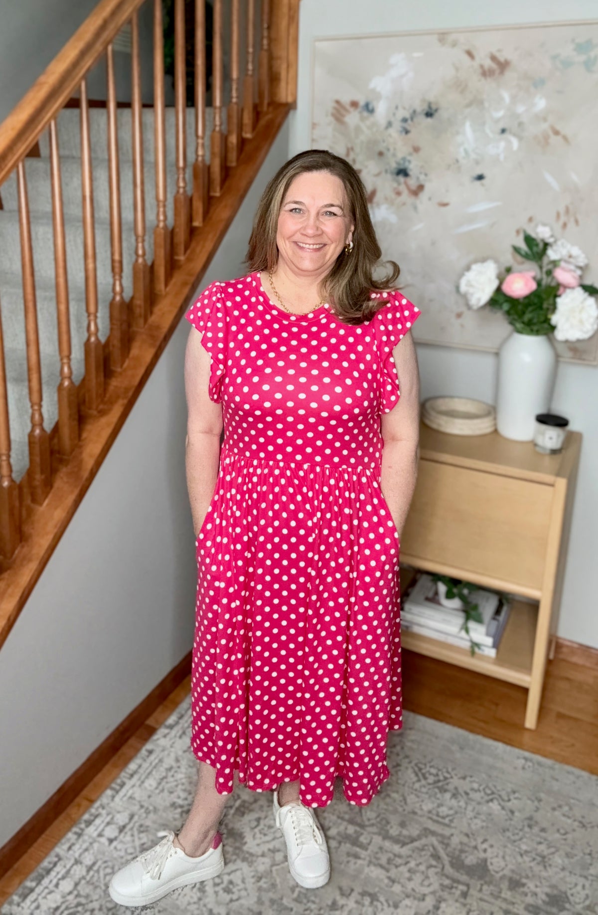 Woman in a pink polka dot dress standing in a home interior.