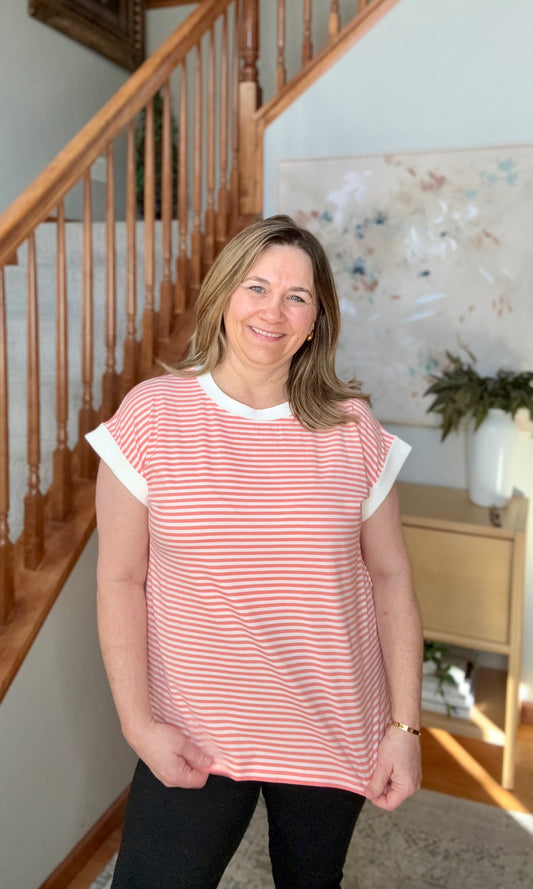 Woman wearing a coral striped shirt standing in a home setting with a staircase and decor.