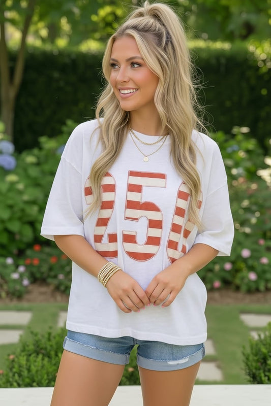 Woman wearing a white t-shirt with red text and denim shorts outdoors.