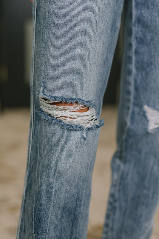 Close-up of a pair of blue jeans with a ripped knee on a blurred background