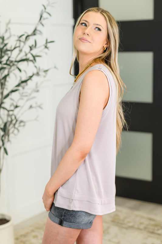 Woman wearing a light gray sleeveless top and denim shorts indoors.