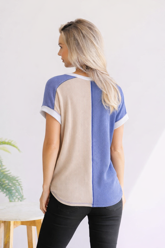 Woman wearing a color-blocked shirt with beige and blue design, standing against a white background.