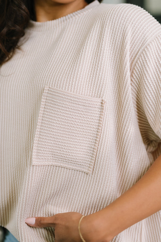 Close-up of a person wearing a beige textured sweater with a pocket.