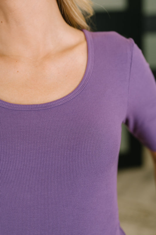 Close-up of a person wearing a short-sleeve ribbed scoop-neck top in a muted purple color.