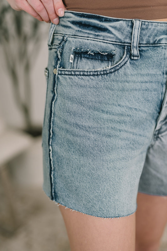 Close-up of a person wearing light blue denim shorts with a blurred background