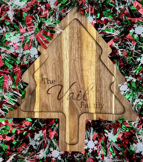 Wooden cutting board shaped like a Christmas tree with 'The Vail Family' engraving, surrounded by festive confetti.