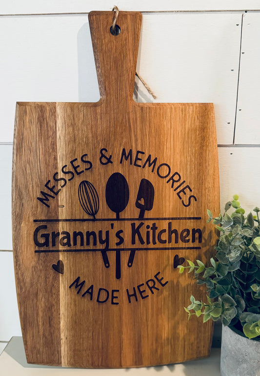 Wooden cutting board with engraved text 'Messes & Memories Granny's Kitchen Made Here' on a white background.