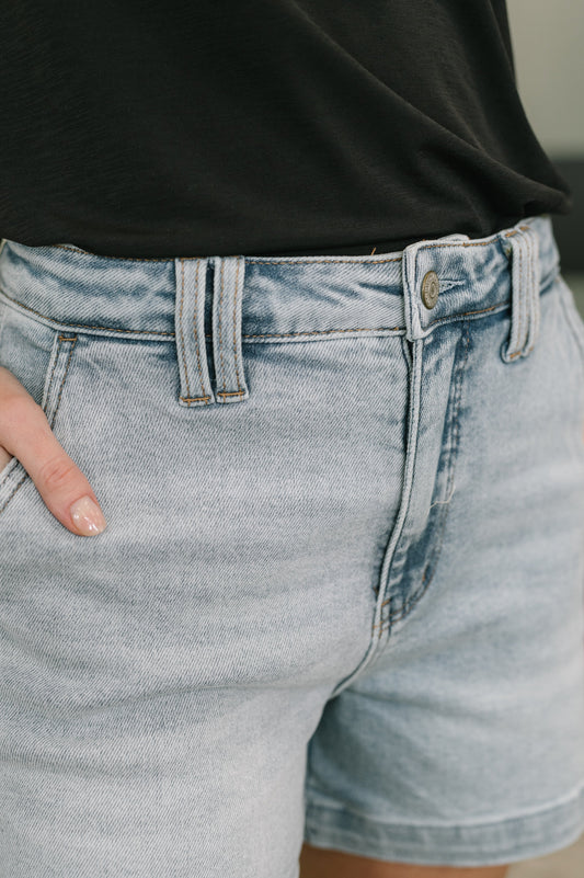 Close-up of light blue denim shorts with a black top worn by a person.