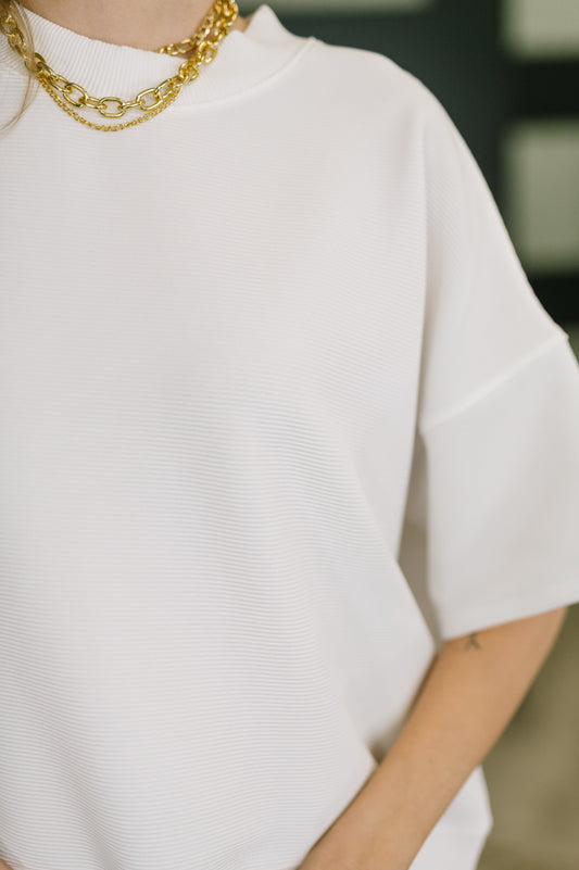 Person wearing a white shirt and gold chain necklace with a blurred background