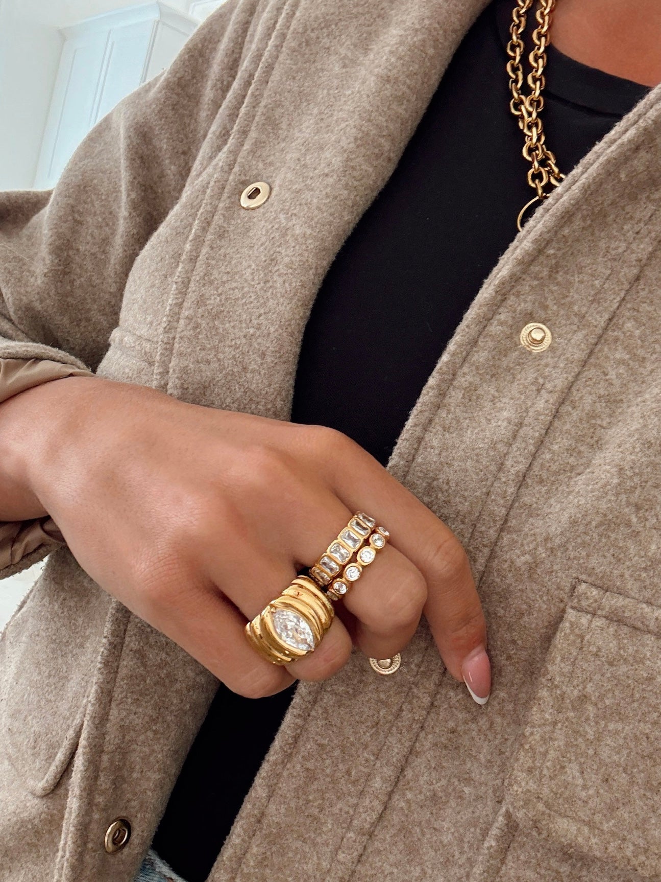 Close-up of a person wearing gold rings and a necklace, with a beige coat.