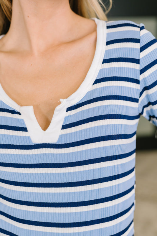 Close-up of a person wearing a ribbed short-sleeve henley top with horizontal light blue, navy, and white stripes.