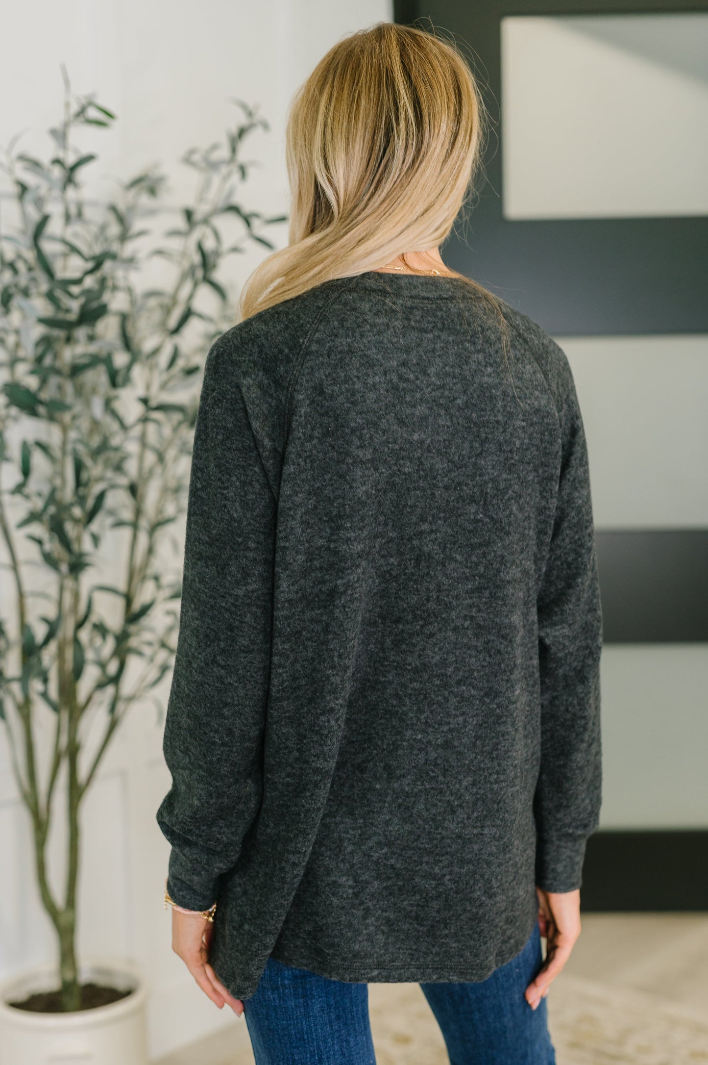 Person wearing a black sweater in an indoor setting with a plant and abstract art in the background.