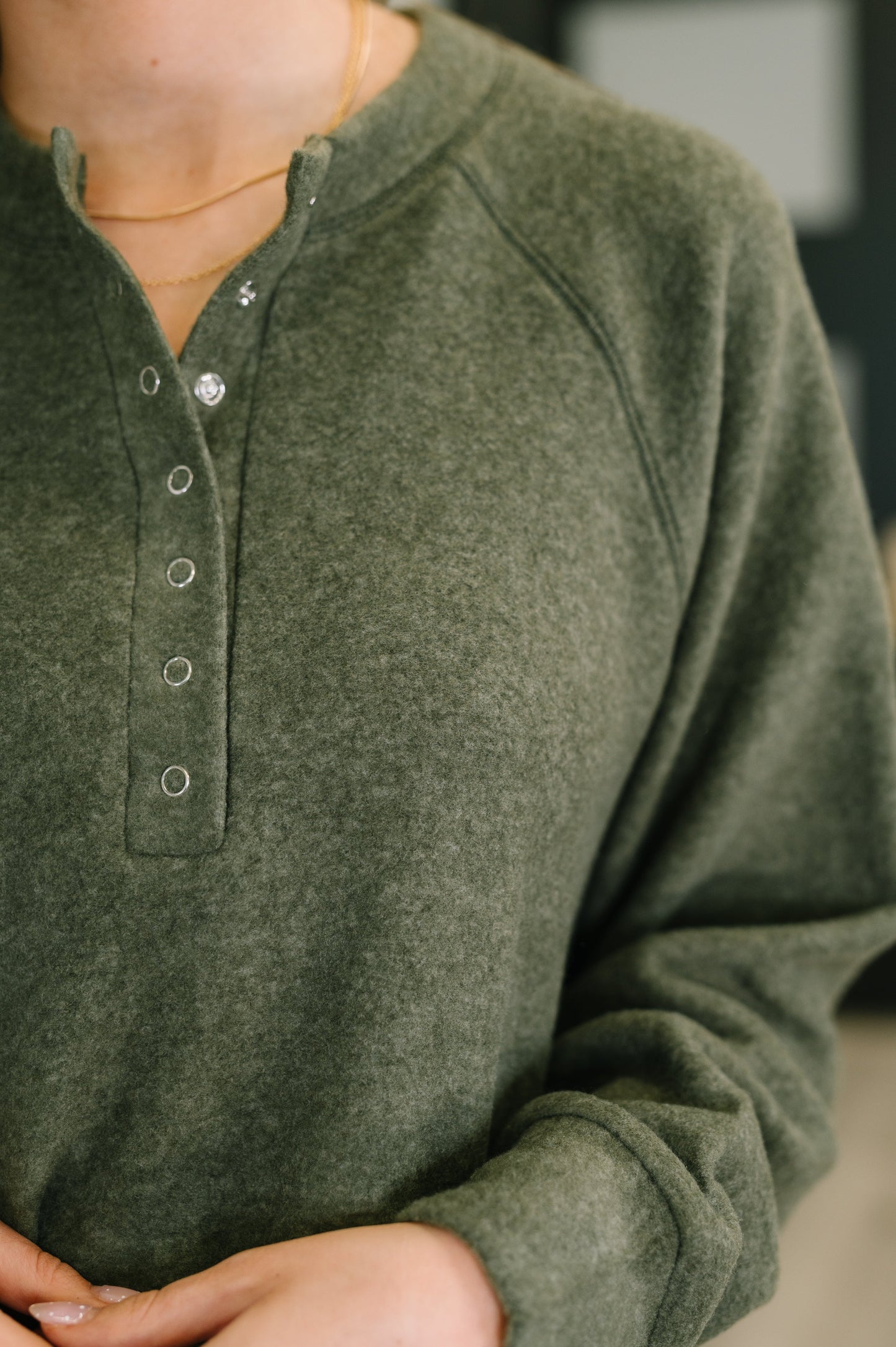 Close-up of a person wearing an olive henley snap green long-sleeve shirt with buttons.