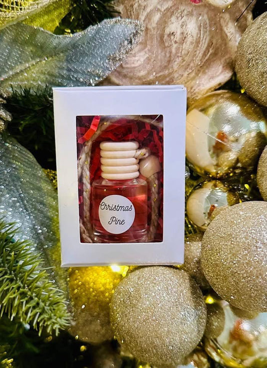 Decorative car diffuser bottle labeled 'Christmas Pine' in a box, surrounded by festive ornaments.