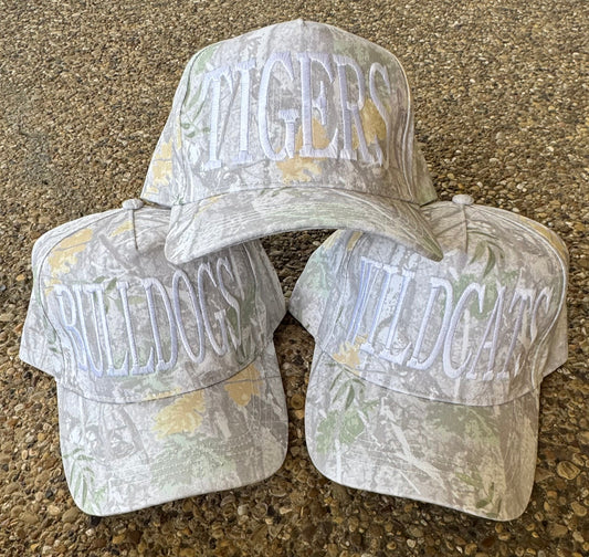 Three camouflage baseball caps with embroidered text on a textured surface