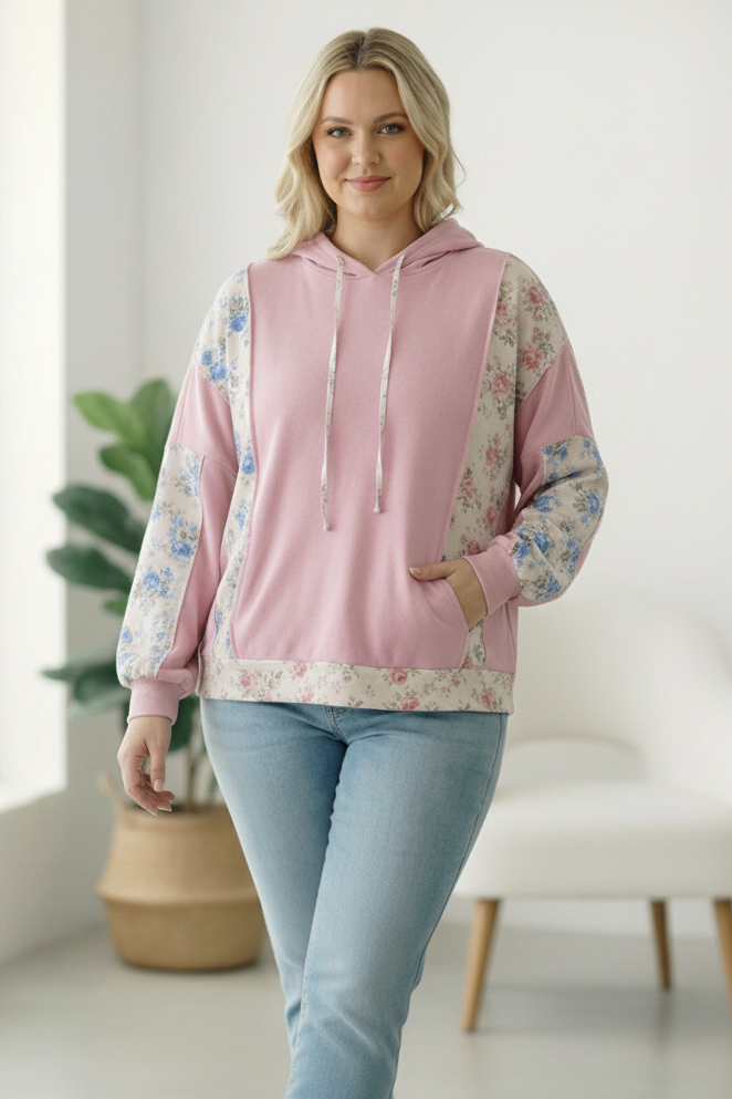 Woman wearing a pink hoodie with floral sleeves in a bright room.