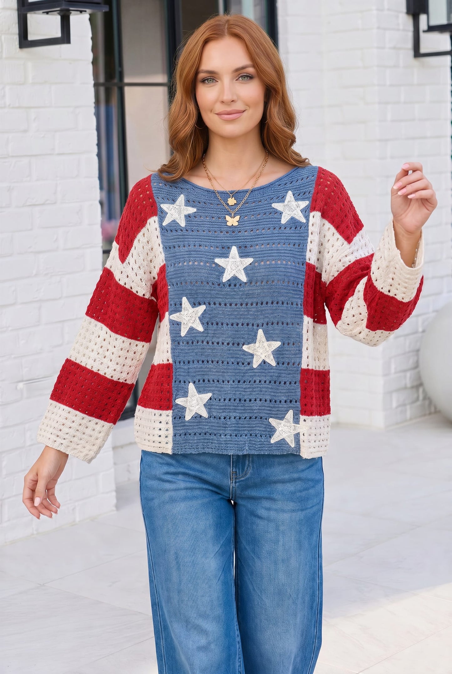 Woman wearing a colorful crochet sweater with star patterns in front of a white brick wall.