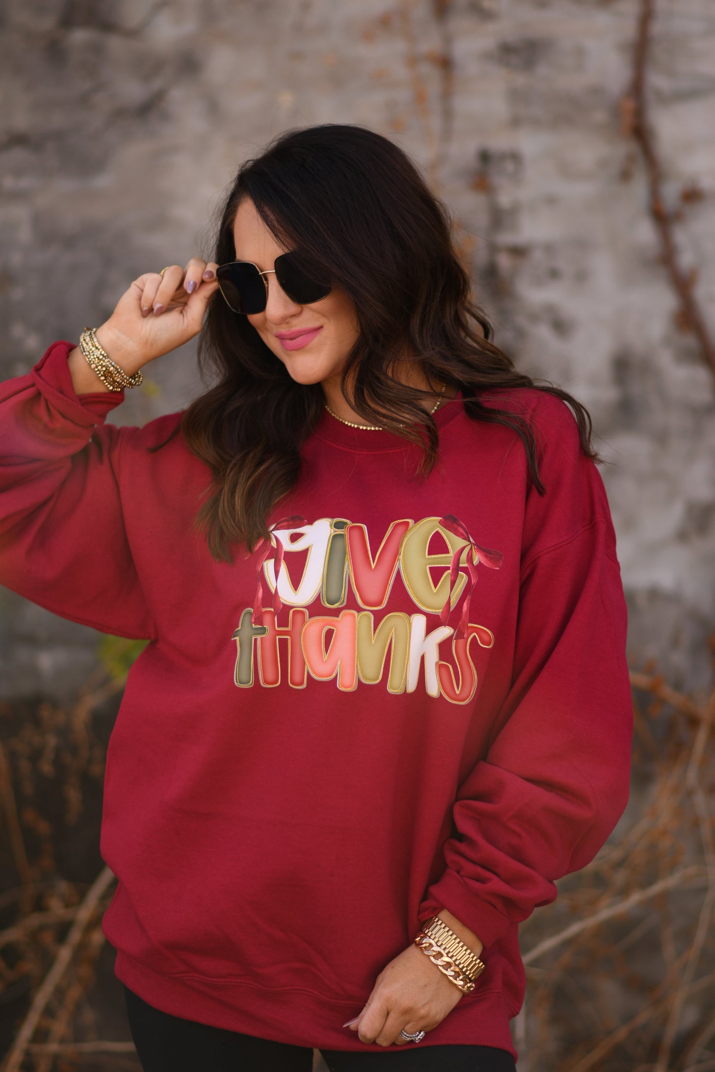 Woman wearing a red sweatshirt with 'Give Thanks' text, standing against a stone wall.