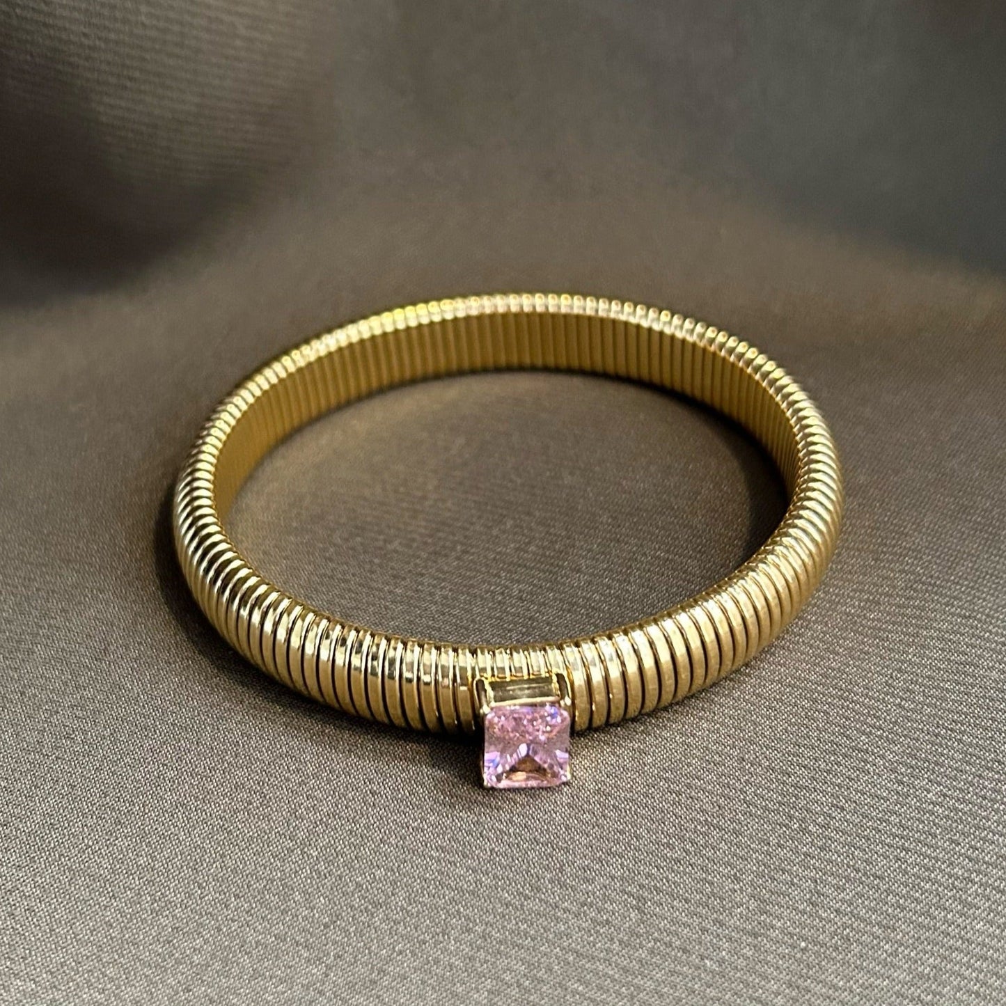 Gold bracelet with a pink gemstone on a gray background
