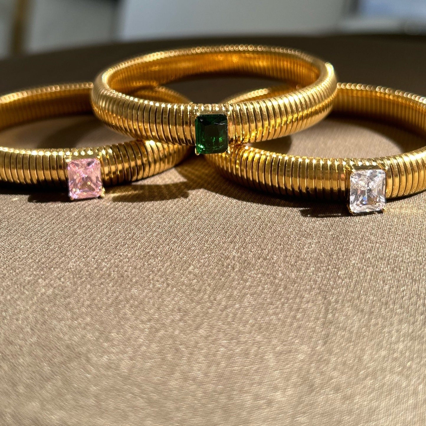 Three gold bangles with gemstones on a beige surface