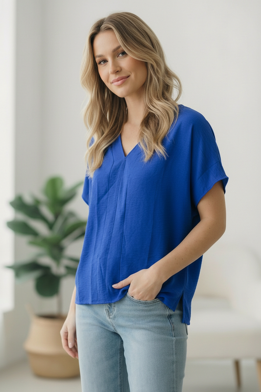 Woman wearing a blue top and light blue jeans indoors with a plant in the background