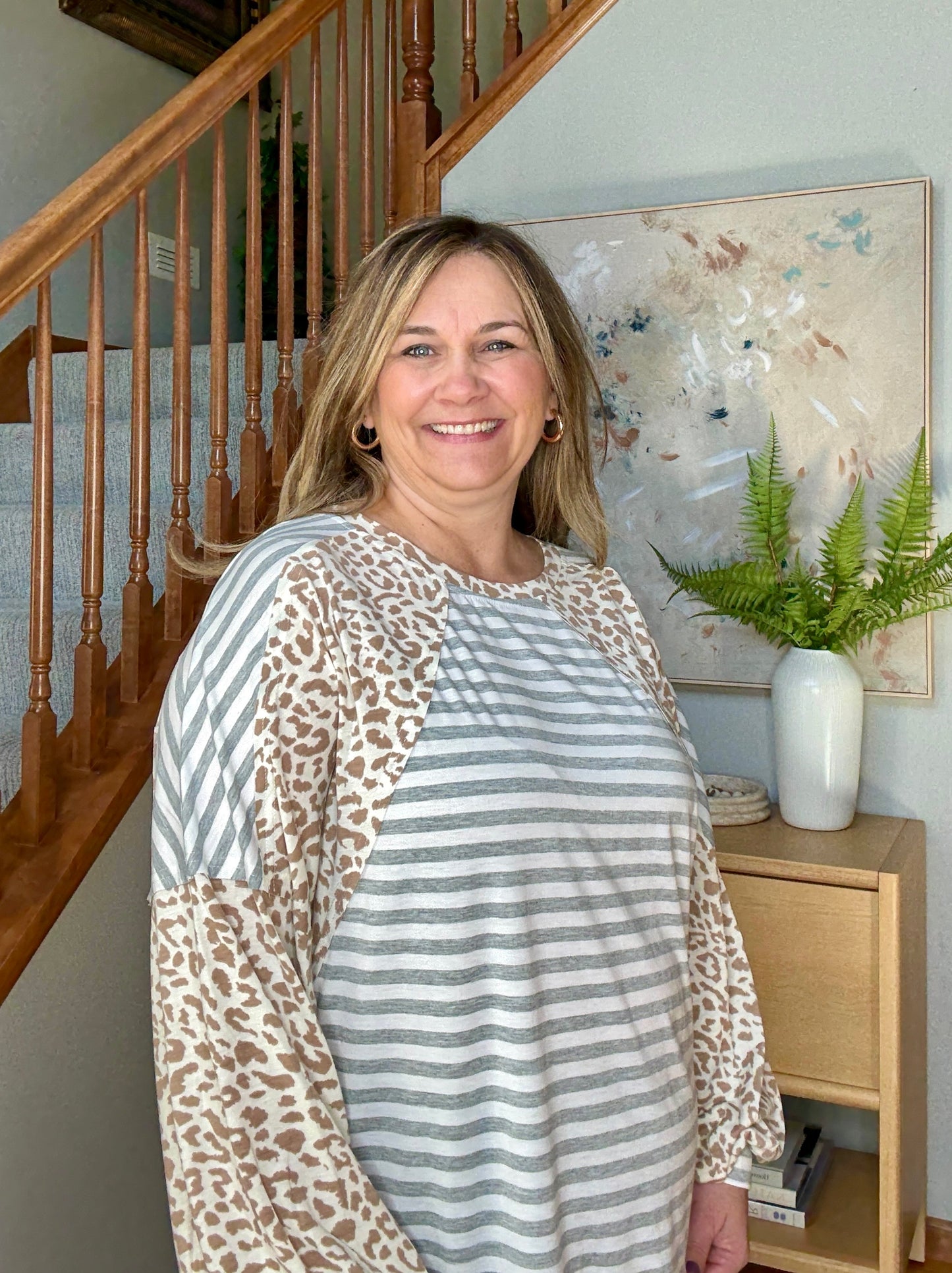 Woman wearing a patterned shirt standing in a home interior with a staircase and decor.