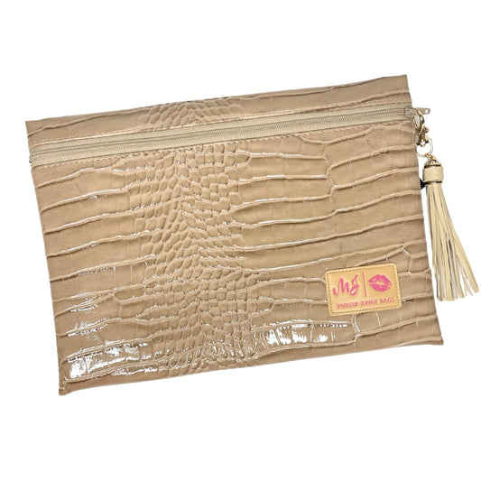 A beige faux-crocodile-embossed zip pouch with a cream tassel zipper pull and a small tan brand patch reading 'vhs makeup bag' with pink lipstick kiss marks, shown on a plain white background.