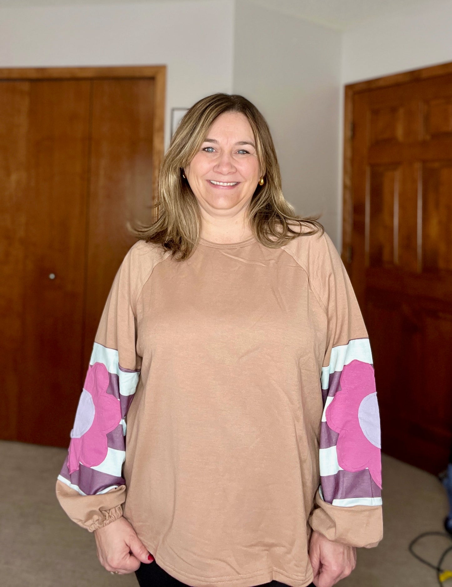 Woman wearing a floral patchwork boho top with floral sleeves in a room with wooden doors.