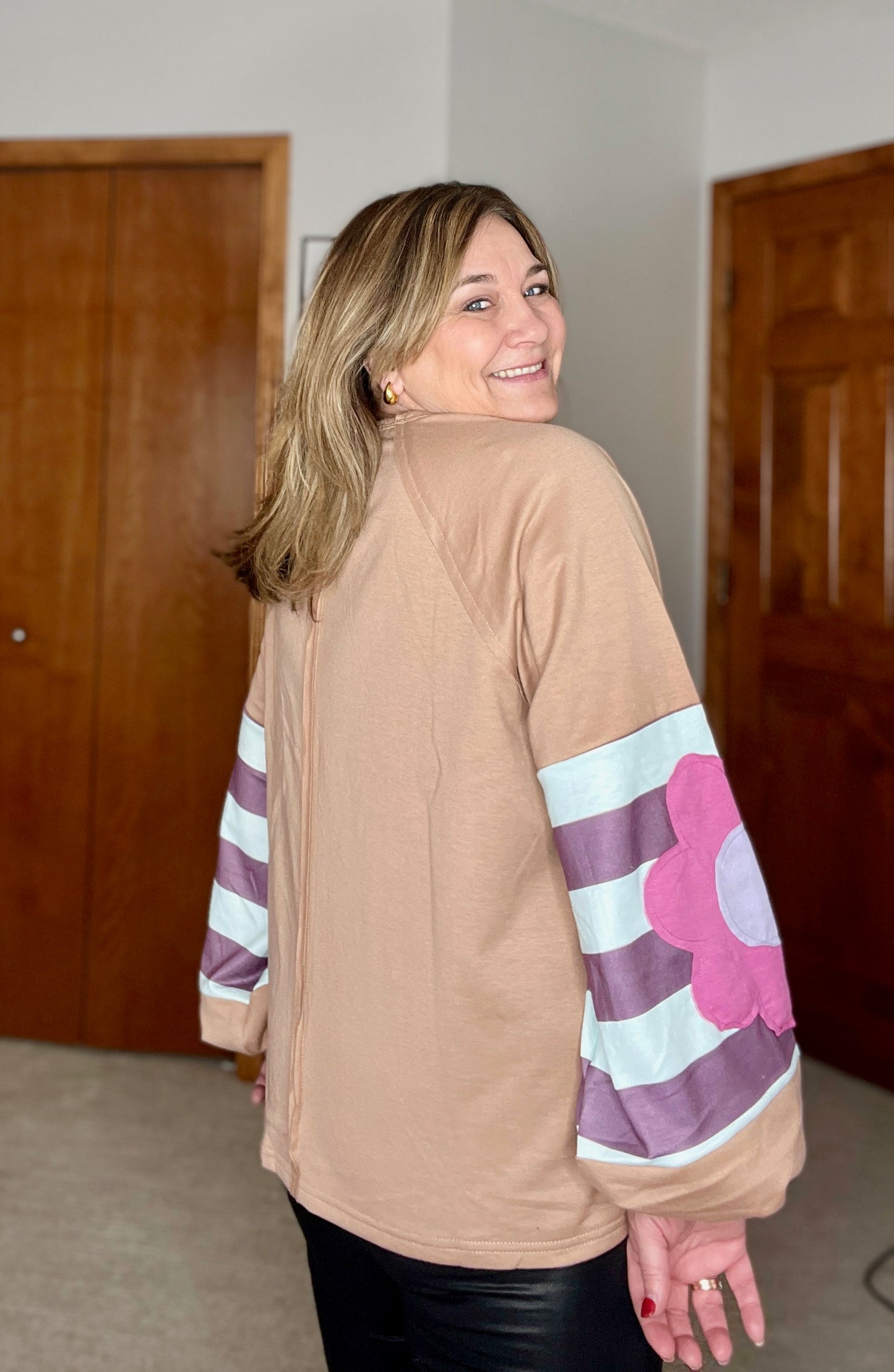 Woman wearing a tan top with colorful sleeves in a room with wooden doors.