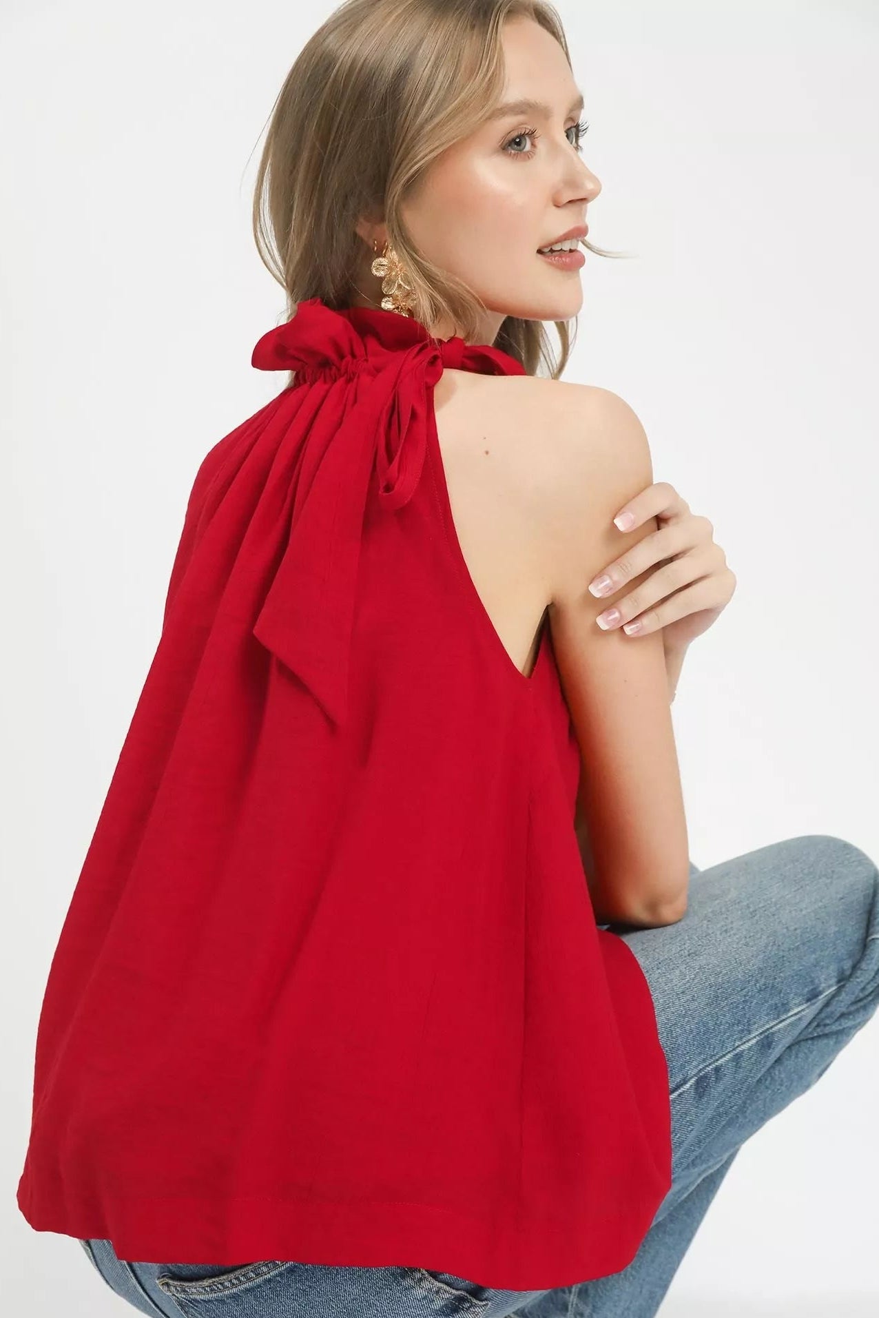 Woman wearing a red halter top with a bow detail, sitting on a white background.