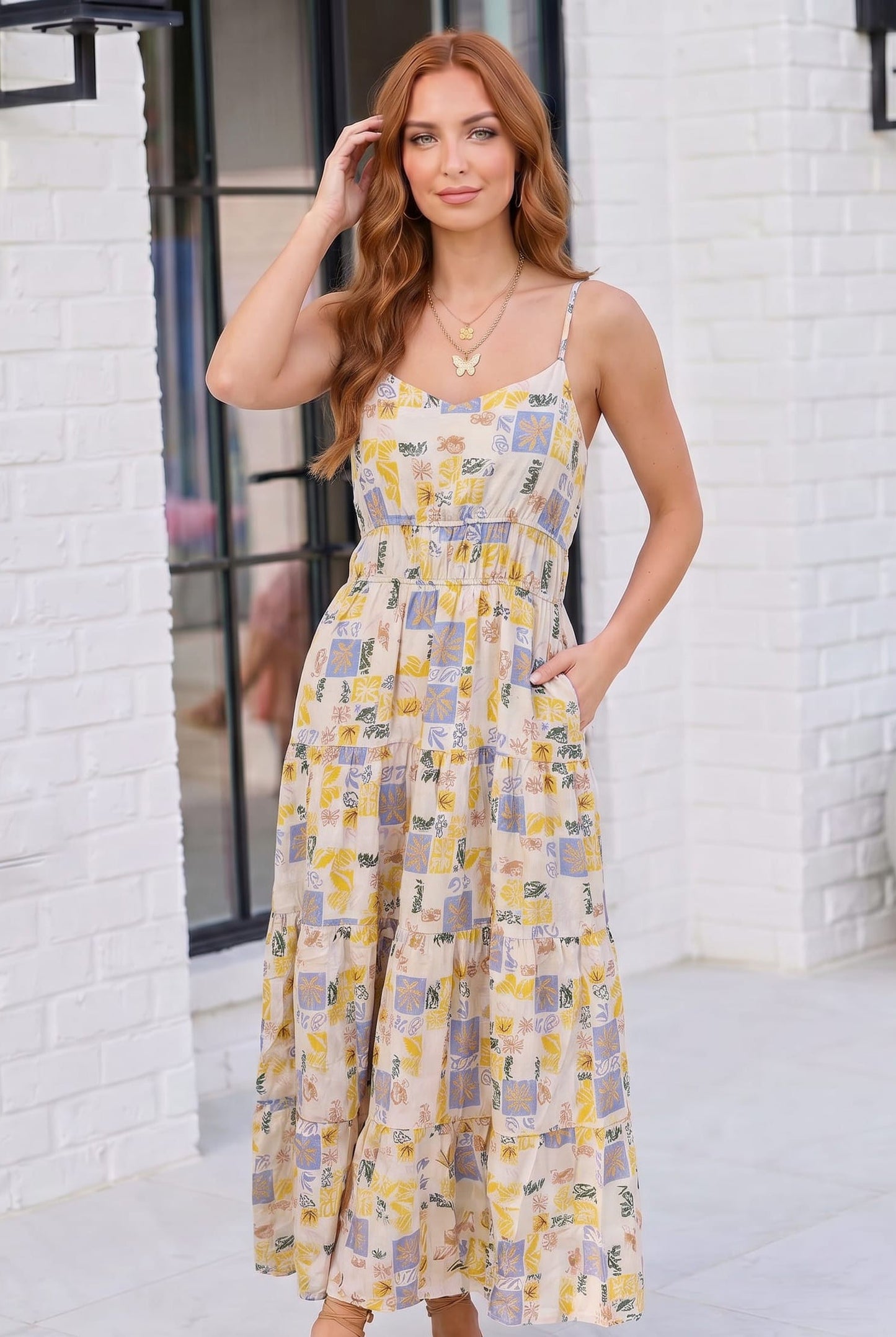 Woman wearing a patterned dress standing against a white brick wall.