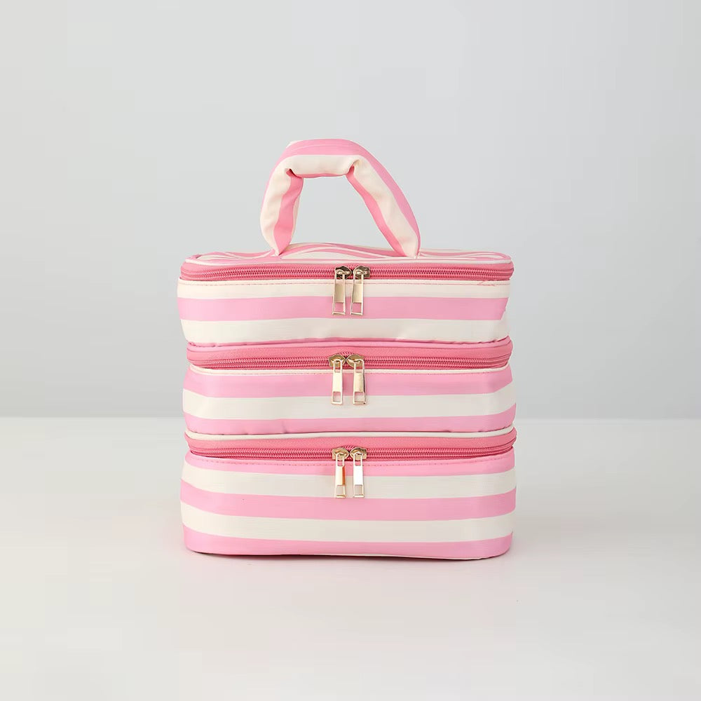Three stacked rectangular zippered cosmetic bags with a pink and white striped pattern and a top handle, shown on a light gray studio background.