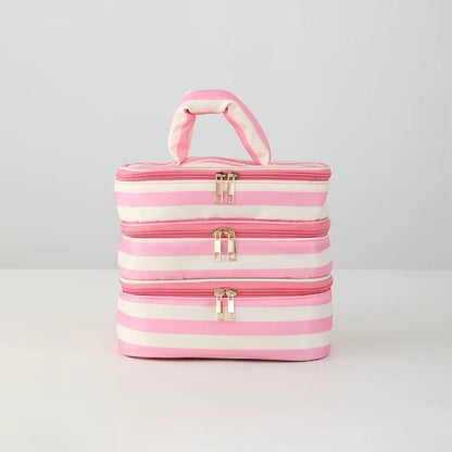 Three stacked rectangular zippered cosmetic bags with a pink and white striped pattern and a top handle, shown on a light gray studio background.