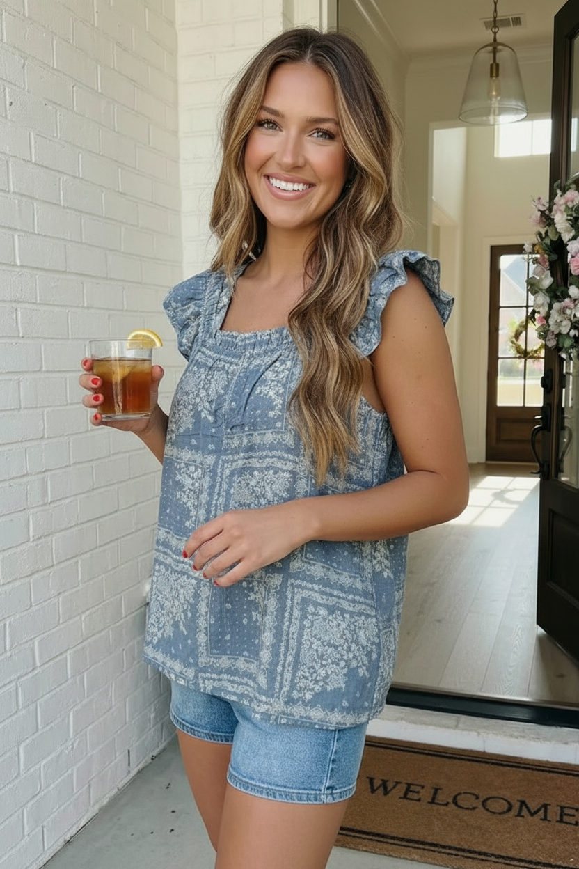 Woman in a blue patterned top and shorts holding a drink, standing in a doorway.