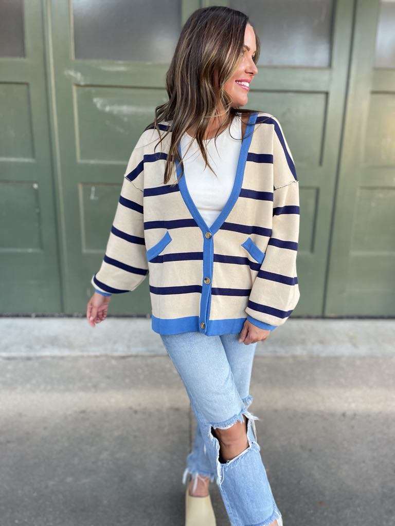 A woman wearing a navy stripe cardigan with contrasting blue buttons and a vest, paired with a white top and blue jeans.