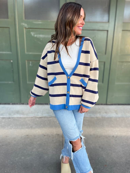 A woman wearing a navy stripe cardigan with contrasting blue buttons and a vest, paired with a white top and blue jeans.